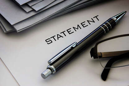 Auf einem Blatt Papier steht das Wort "STATEMENT", daneben liegt ein grauer Kugelschreiber und eine dunkelrandige Lesebrille