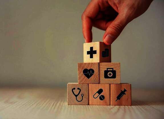 Eine Hand, die eine Pyramide mit Würfel gestapelt hat.. Die Würfel sind mit Pflegesymbole (Spritze, Herz, Tablette ....) bedruckt.