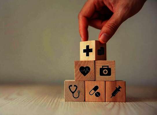 Eine Hand, die eine Pyramide mit Würfel gestapelt hat.. Die Würfel sind mit Pflegesymbole (Spritze, Herz, Tablette ....) bedruckt.