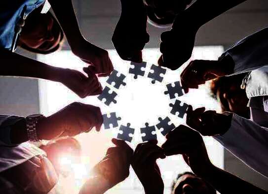 Pflegekräfte stehen im Kreis und halten jeweils ein Puzzle-Teil in die Mitte