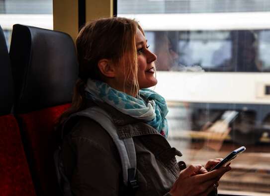 Frau sitzt im Zug und hat Handy in der Hand