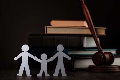 Gesetzeshammer angelehnt an Bücherstapel. Davor als Scherenschnitt eine Familie bestehend aus zwei Erwachsenen und einem Kind