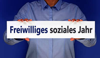 Person, deren Gesicht nicht sichtbar ist und die ein Schild mit der Aufschrift "Freiwilliges Soziales Jahr" in die Kamera hält