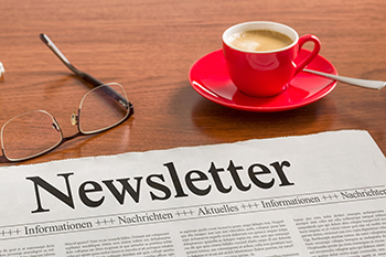 Zeitung mit der Überschrift Newsletter auf einem hölzernen Tisch neben einer roten Kaffeetasse